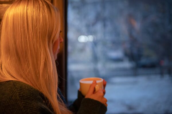 Mujer joven junto a una ventana con expresión tranquila, tomando un descanso para respirar y calmar la ansiedad cotidiana.